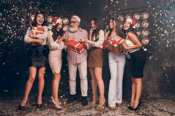 Santa give gifts for girls. Happy New year with presents and Santa Claus. Modern bearded man in Santa's hat with beautiful girls in club with gold confetti celebrate New Year and Christmas party 2018