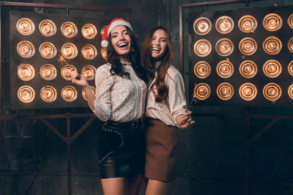Zwei glückliche schöne Mädchen in Weihnachtsmannmütze mit Bengalischen Lichtern tanzen und Spaß haben. Weihnachtsfeier mit meiner besten Freundin. Neues Jahr 2018 — Stockfoto