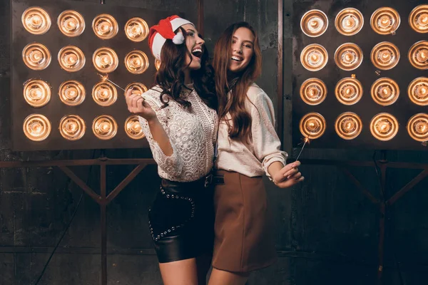 Zwei glückliche schöne Mädchen in Weihnachtsmannmütze mit Bengalischen Lichtern tanzen und Spaß haben. Weihnachtsfeier mit meiner besten Freundin. Neues Jahr 2018 — Stockfoto