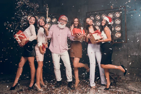 All they need is fun. Modern bearded man in Santa's hat carrying Christmas bengal lights with beautiful girls in club with gold confetti celebrate New Year and Christmas party 2018 — Stock Photo, Image