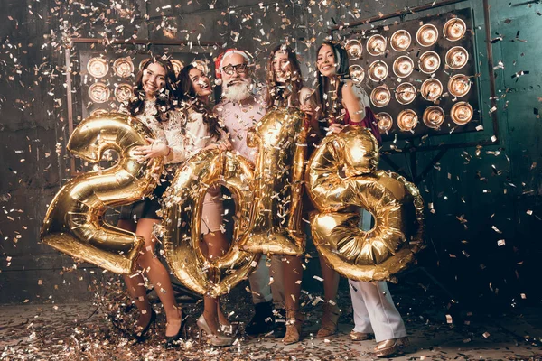 Feliz Natal com os amigos. Grupo de garotas atraentes com homem barbudo em camisa rosa e chapéu de Papai Noel se divertir com números coloridos de ouro de 2018 Ano Novo . — Fotografia de Stock