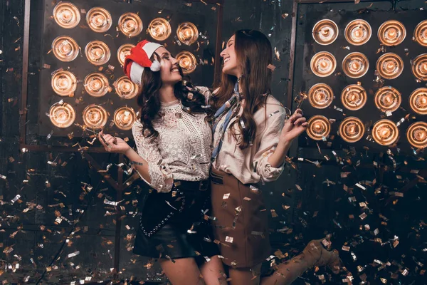 Duas meninas bonitas felizes no chapéu de Papai Noel com luzes de bengala dançando e se divertir em ouro e prata confete. Festa de Natal com o meu melhor amigo. Ano Novo 2018 — Fotografia de Stock