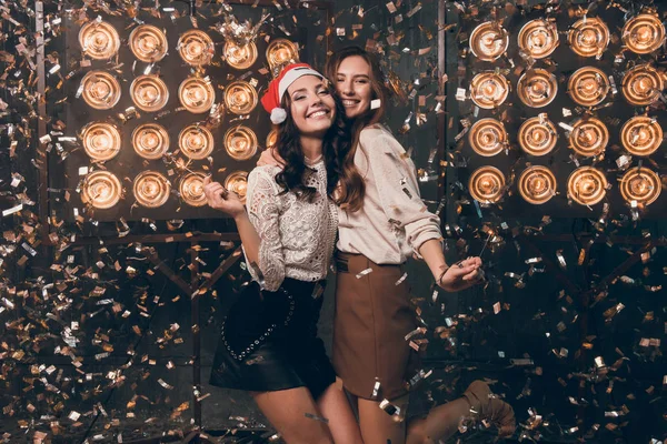 Duas meninas bonitas felizes no chapéu de Papai Noel com luzes de bengala dançando e se divertir em ouro e prata confete. Festa de Natal com o meu melhor amigo. Ano Novo 2018 — Fotografia de Stock