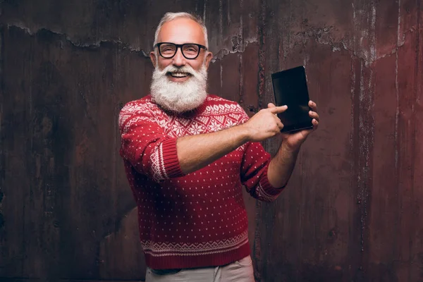 Un hombre mayor feliz moderno usando un teléfono inteligente en un suéter de Navidad. Santa Claus desea Feliz Navidad —  Fotos de Stock