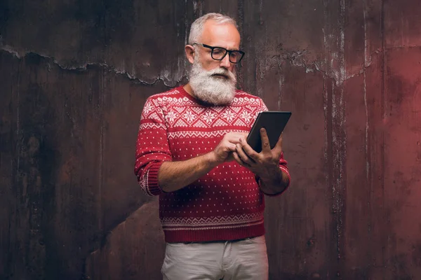 Un hombre mayor moderno usando un teléfono inteligente en un suéter de Navidad. Santa Claus desea Feliz Navidad —  Fotos de Stock