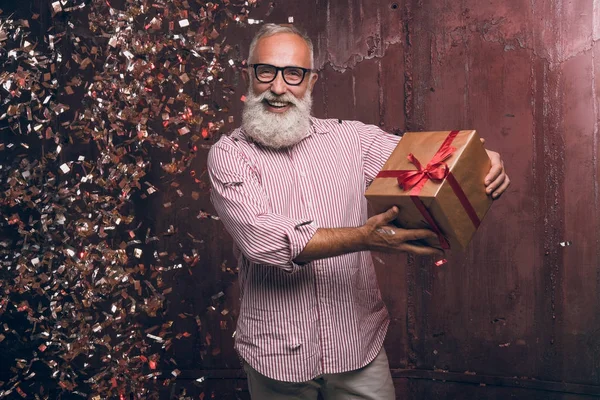 Modern senior bearded man gives a gift and happy smile in gold confetti. Happy New Year 2018. Merry Christmas to you! — Stock Photo, Image