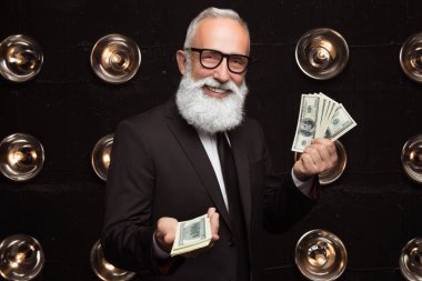 Mutlu sakallı insan taşımak dolar ve gülümseme, birçok banknot taşıyan formal giyim ve moda gözlük. Kamera arıyorum. Mutlu para ödülü.