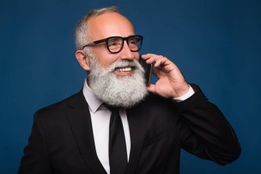 Mutlu gülümseyen iş takım elbiseli telefonda konuşurken bir akıllı telefon ile adam sakallı. Telefon iş konuşma ortak veya Yöneticisi 