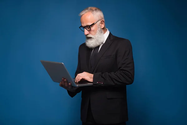 Concéntrese barbudo senior y hombre de negocios quedarse con el cuaderno y trabajar aislado sobre un fondo azul. Trabajador hombre de negocios en traje recto y gafas —  Fotos de Stock