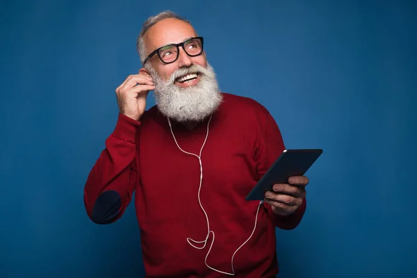Expectation from a new song. Happy modern bearded man listening a new music from tablet. Man with headphones listen to music isolated on blue background