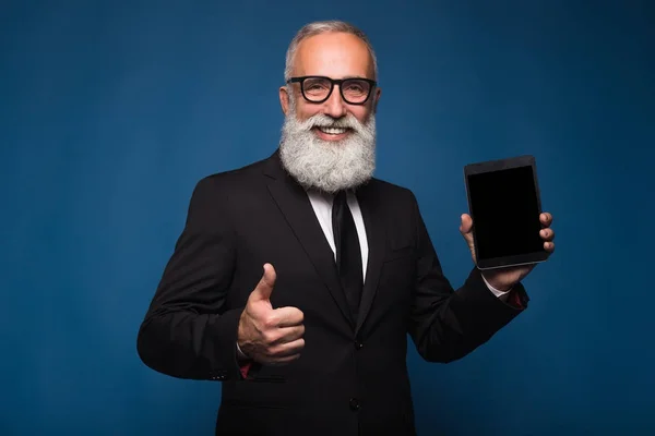 Hombre barbudo feliz en desgaste formal sostiene tableta digital y muestra espacio de copia en la pantalla mientras está de pie sobre fondo azul. Lugar vacío de la pantalla de la tableta. Hombre espectáculo con la pantalla de la tableta y el pulgar hacia arriba —  Fotos de Stock