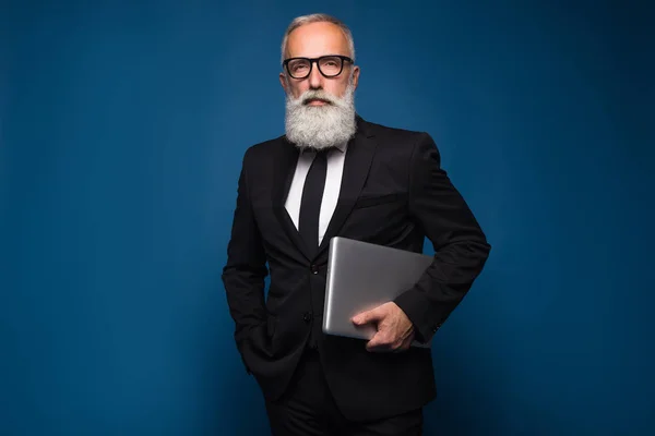 Concéntrese barbudo senior y hombre de negocios quedarse con el cuaderno y trabajar aislado sobre un fondo azul. Trabajador hombre de negocios en traje recto y gafas —  Fotos de Stock