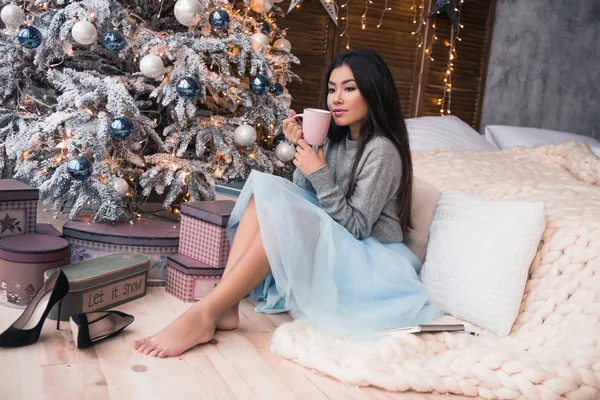 Bonne année à vous ! belle asiatique fille se trouve près de arbre de Noël et boit café . — Photo