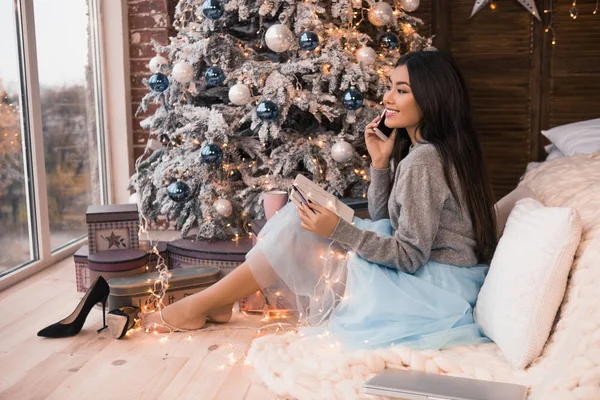 Christmas letter writing on notebook and talking on the phone. Many garlands. Christmas , winter holidays and people concept. Girl writes her wish