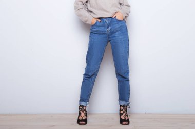 Fashion jeans on a girl. Thin legs of fashion girl. Shapely female legs in high heel shoes and jeans near a white wall  clipart