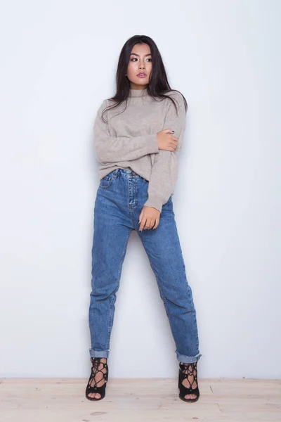 Portrait of looking away serious girl which touch her sweeter and fashion posing on white background.Styling wearing girl in a jeans, shoes and sweeter — Stock Photo, Image