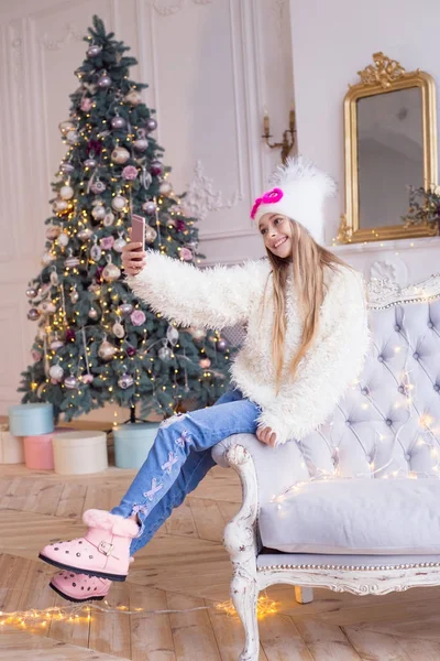 Petite fille heureuse félicite ses amis pour Noël et le Nouvel An sur la communication vidéo dans les réseaux sociaux. Des vêtements élégants et à la mode . — Photo