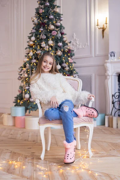 Маленькая счастливая девочка сидит на фоне рождественских украшений в стильной и модной одежде — стоковое фото