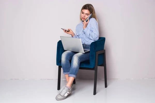 Ошеломленная деловая женщина, сидящая на стуле. Слишком много звонков за один день. Два телефона и ноутбук . — стоковое фото