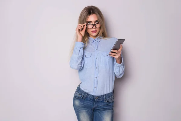 Photo of young serious business woman in glasses over grey wall looking at camera and using phone. — Stock Photo, Image