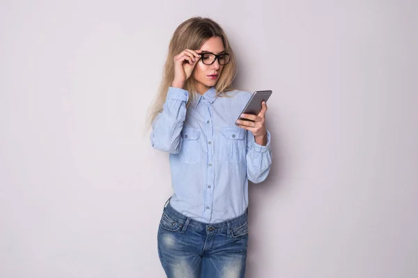 Photo of young serious business woman in glasses over grey wall looking on phone. — Stock Photo, Image