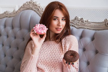 Bir kız çörek tutuyor. Pembe ve çikolata krema ile iki lezzetli kek. Gülümseyen ve gülüyor.