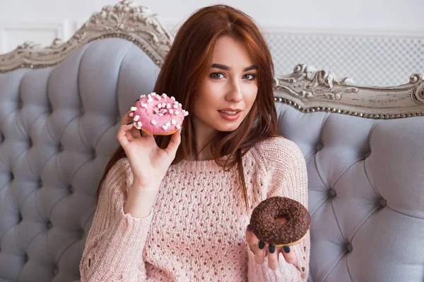 Una chica tiene rosquillas. Dos deliciosos pasteles con crema rosa y chocolate. Sonriendo y riendo . — Foto de Stock