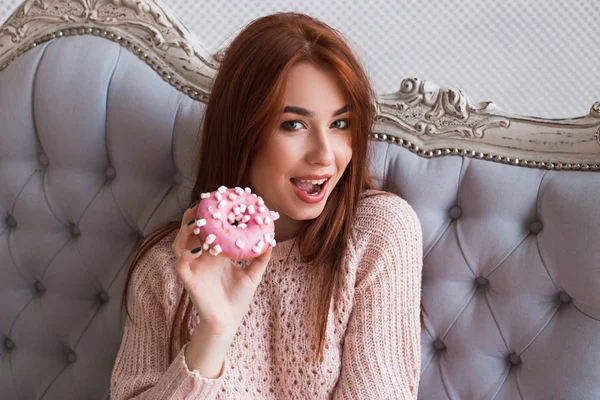 Uma rapariga está a segurar um donut. Um delicioso bolo com creme rosa. Sorrindo e rindo . — Fotografia de Stock