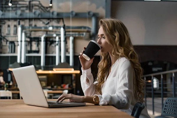 Женщина работает над своим ноутбуком. Она ищет информацию в сети Интернет. Женщина пьёт кофе. Рабочий день . — стоковое фото