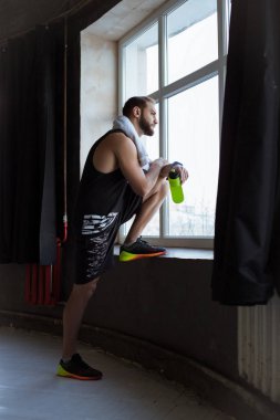 Sportif etkin adam elinde şişe ile spor penceresinde yakınındaki kalmak ve uzak arıyorum.