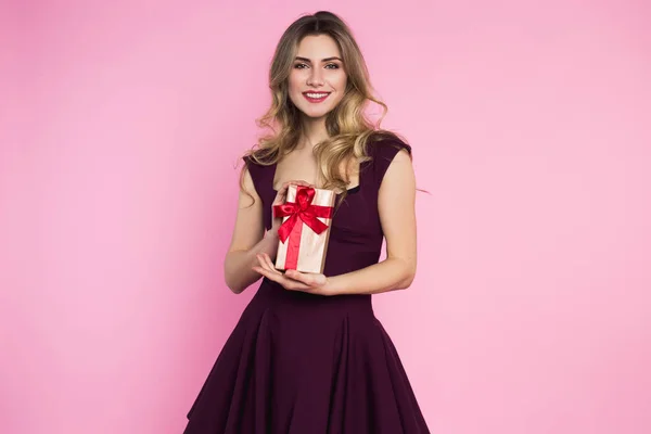Menina bonita e encantadora está segurando uma pequena caixa com um presente na mão. Fundo rosa. Dia da mulher feliz — Fotografia de Stock