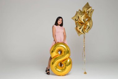 Pembe elbiseli çekici, güzel Asyalı kız büyük altın balon tutuyor. Yıldız şeklinde balonlar.