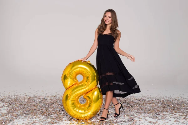 Sexy, menina bonita em vestido preto está segurando grande dourado 8 em forma de balão. Confetti. . — Fotografia de Stock