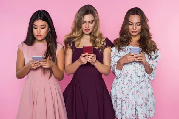 Три красивые, милые дамы и болтовня на их смартфонах. Розовый фон . — стоковое фото