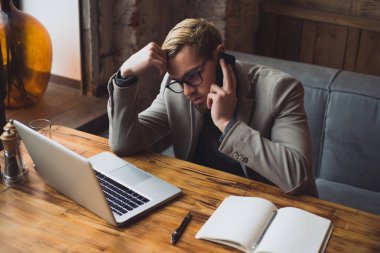 Yorgun iş adamı telefonda konuşurken ve proje hakkında düşünüyor. Kafede dizüstü bilgisayarda çalışma.