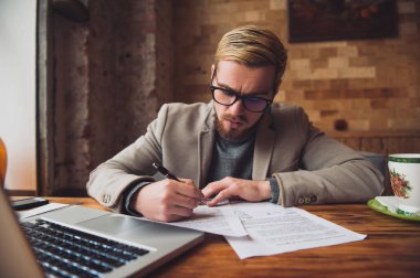 Genç meşgul adam belgeleri imzalama ve dizüstü bilgisayarda çalışma.