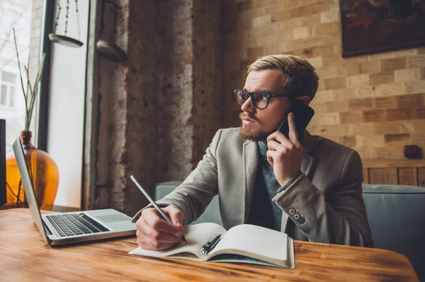 Hombre de negocios guapo hablando por teléfono en un café y anotando las notas  . —  Fotos de Stock