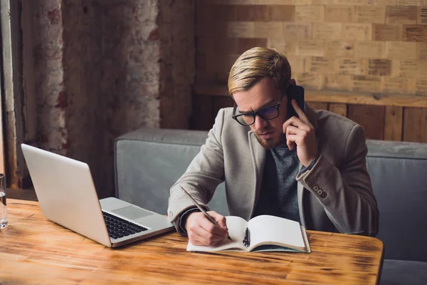 Hombre de negocios está teniendo una conversación en su teléfono inteligente y tomando notas . —  Fotos de Stock