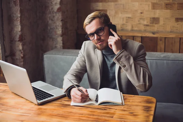 Hombre de negocios feliz está teniendo una conversación en su teléfono inteligente y tomando notas . —  Fotos de Stock