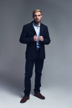 Başarılı ve yakışıklı. Gri arka plan önünde lapels duran tutan genç iş adamı