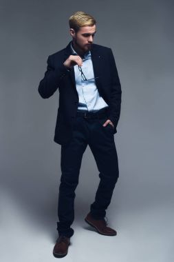 Şık ve profesyonel. Gözlük tutan ve gri arka plan önünde cep içine diğer el koymak moda girişimci tam uzunlukta bir portresi.