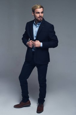 Profesyonel ve şık. Lapels ceketinin gri arka plan önünde tutan bir iş adamı tam uzunlukta bir portresi.