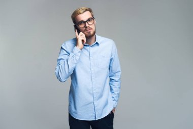 Ciddi ve yakışıklı. Genç iş adamı meslektaşı için onun cep telefonuyla konuşuyor. Gri arka plan.