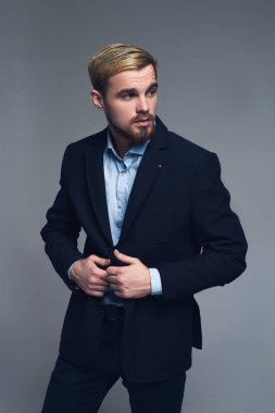 Ciddi ve profesyonel. Ayakta ve gri arka plan önünde izlerken lapels tutan genç iş adamı