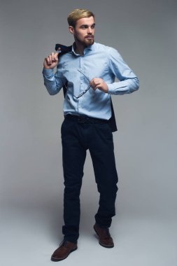 Yakışıklı ve profesyonel. Ceket omuz gri arka plan önünde tutan başarılı kişi tam uzunlukta bir fotoğrafı.