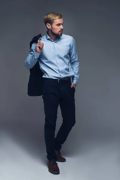 Μοντέρνο και επαγγελματικό. Μοντέρνος επιχειρηματίας κρατώντας σακάκι του στον ώμο και να θέσει το άλλο χέρι στην τσέπη μπροστά σε γκρι φόντο. — Φωτογραφία Αρχείου