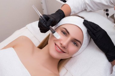 Kendine iyi bak! Genç gülümseyen kadın klinik kozmetik yordamda olarak yüz maskesi alma.