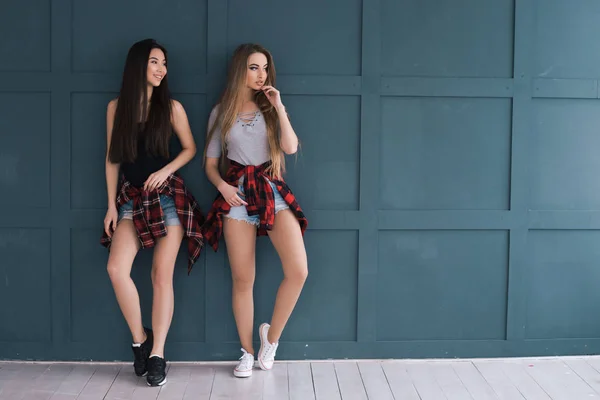 Modelleren is een levensstijl! Twee volle lengte portret van jonge vrouwen het dragen van casual kleding en permanent tegen de blauwe achtergrond. — Stockfoto