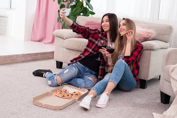 Deixe os bons tempos rolar! Jovens senhoras alegres fazendo selfies enquanto bebem vinho e desfrutam de seu tempo de lazer em casa . — Fotografia de Stock