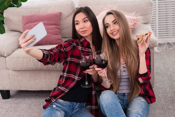 Une amitié à vie ! Merveilleux jeunes meilleurs amis faisant différentes photos tout en buvant du vin rouge, ils s'assoient sur le sol et se penchent sur un canapé beige . — Photo